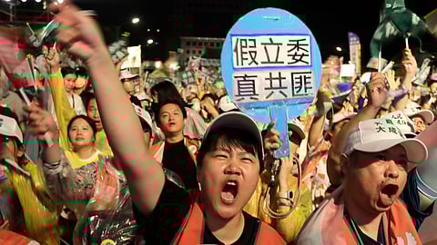 People shoot behind a slogan reading ''Fake Legislators Are Real Communist Bandits'' during a campaign rally to promote recall vote targeting 24 Nationalist Party (KMT) lawmakers in Taipei, Taiwan, Thursday, July 24, 2025.