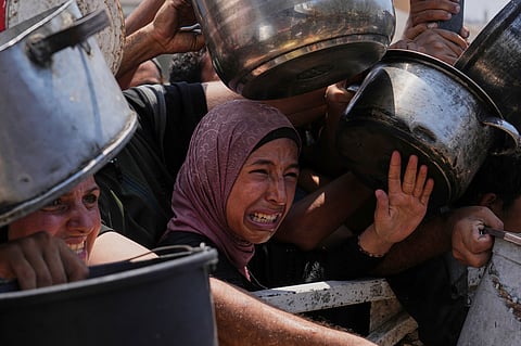 Palestinians struggle to get donated food at a community kitchen, in Gaza City, northern Gaza Strip, Saturday, July 26, 2025.
