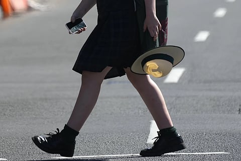 A school girl holds her phone while crossing a street in Sydney, on Nov 8, 2024.