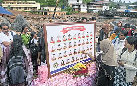 Teachers of Vellarmala GVHSS place flowers in front of the photos of students who lost their lives in the Chooralmala- Mundakkai landslide, during a commemoration service held near Bailey bridge