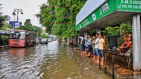 People wait for buses at a stop during rain, in Jaipur, Wednesday, July 30, 2025.