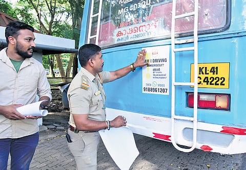 An MVD officer pasting a sticker on a private bus at Kakkanad. The sticker displays a WhatsApp number through which people can directly send photos and videos of traffic rule violations to the department