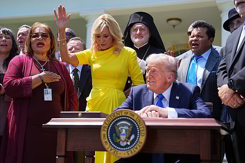President Donald Trump sits at a desk as he and religious leaders listen to a musical performance before Trump signs an executive order during a National Day of Prayer event in the Rose Garden of the White House, May 1, 2025, in Washington.