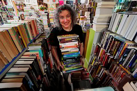 Michelle Souliere, owner of the Green Hand Bookstore, carries a stack of books to the shelves, in Portland, Maine, on Thursday, Aug. 7, 2025.