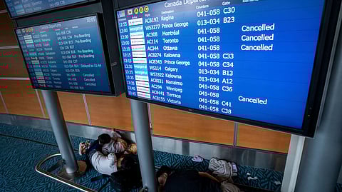 People sleep under a flight information board at the Vancouver International Airport in Richmond, B.C., Canada, on Saturday, August 16.