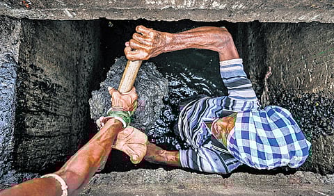 A sanitation worker handing over silt from a drain to another worker, both without any protective gear like gloves and masks in Bhubaneswar