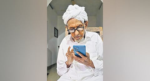 M A Abdullah Maulavi Bafaqi scrolling on his smartphone