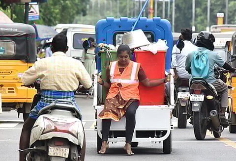 A woman sanitary worker is seen precariously sitting on the edge of a garbage collection vehicle while on duty.