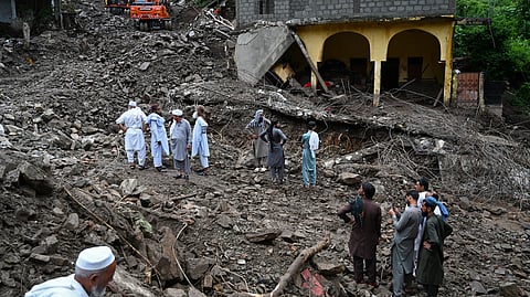 Residents watch as relief personnel search through the rubble of collapsed houses for victims during a rescue operation,