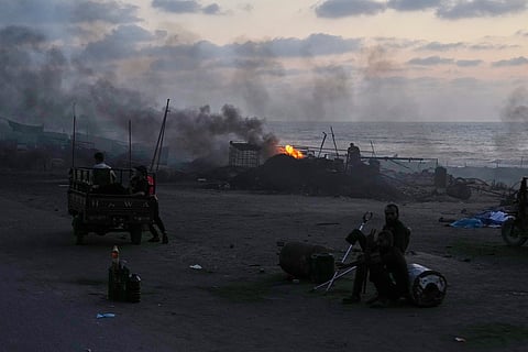 People sit near makeshift burners, used to extract fuel from melted plastic, where displaced Palestinians try to make a living selling homemade fuel along the Sea Road, at dusk in the south of Gaza City.