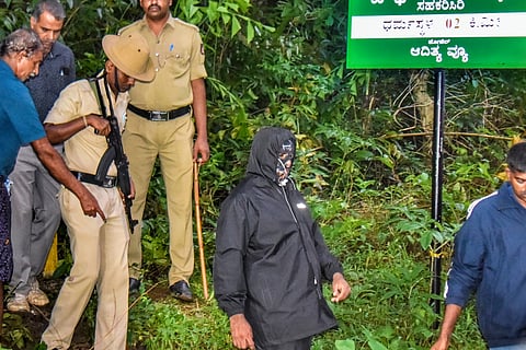 In this Monday, August 4, 2025 file photo, security personnel with the complainant, in mask, near a site of an alleged burial related to the Dharmasthala mass burial case, at Dharmasthala