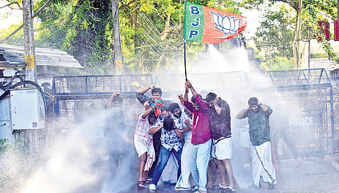 Yuva Morcha workers huddle as police use water cannons during a protest march to Leader of Opposition V D Satheesan’s official residence in Thiruvananthapuram demanding the resignation of Rahul Mamkootathil as Palakkad MLA