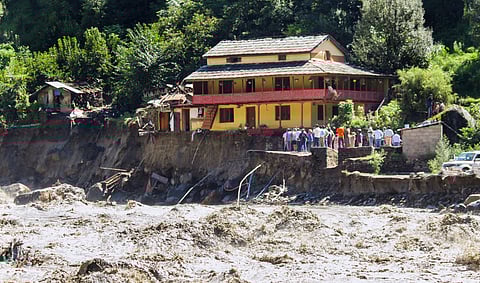 People gather near a house after it was partially washed in the Beas river flowing in spate due to heavy rainfall.