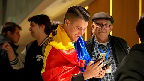 A supporter of the pro-EU Party of Action and Solidarity (PAS) draped in the Moldovan flag smiles as he checks partial results on a phone after the polls closed for the parliamentary election, in Chisinau, Moldova, Sunday, Sept. 28, 2025.