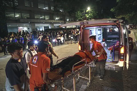 Medical workers load a resident into an ambulance as others stay outside buildings after a strong earthquake struck Cebu city, central Philippines, on Tuesday, Sept. 30, 2025.