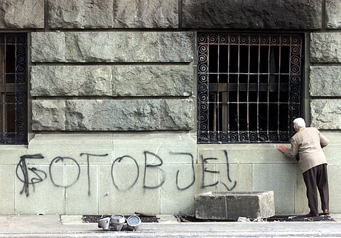 A man inspects the damages to the Yugoslav parliament, next to a graffito reading "You are finished", on October 8, 2000, in central Belgrade.