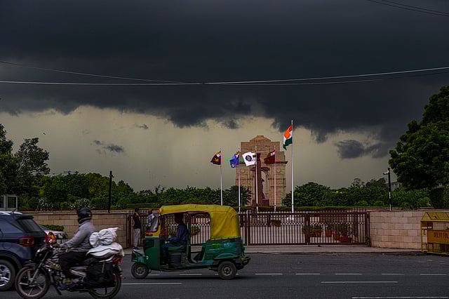 Vehicles pass by the War Memorial as dark clouds cover the skyline above the India Gate, in New Delhi, Tuesday, Oct. 7, 2025.
