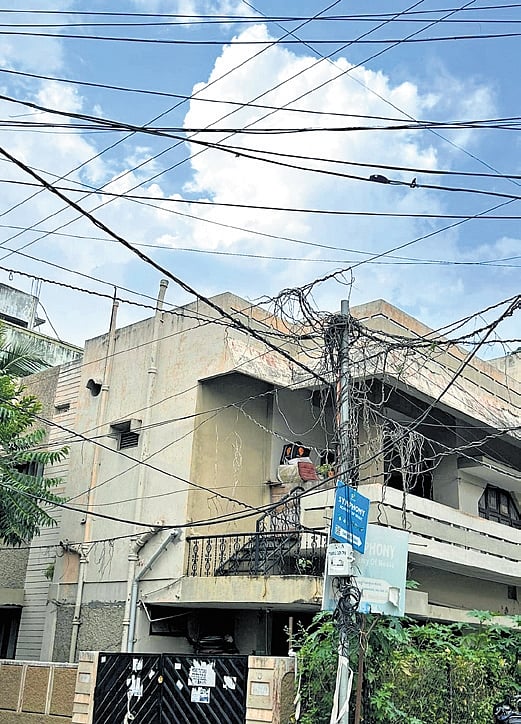 Overhead wires and dangling cables seen hanging over a footpath and near a home in Hyderabad