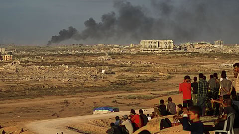 Displaced Palestinians watch smoke rise after Israeli military strikes as they gather on the coastal road near Wadi Gaza, in the central Gaza Strip, Thursday, Oct. 9, 2025.