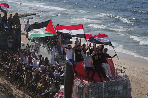 Displaced Palestinians ride on trucks loaded with belongings and wave Egyptian and Palestinian flags as they travel along the coastal road near Wadi Gaza in the central Gaza Strip, moving toward Gaza city, Saturday, Oct. 11, 2025, after Israel and Hamas agreed to a pause in their war and the release of the remaining hostages.