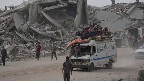 Displaced Palestinians ride on a van loaded with their belongings amid rubble in Gaza City, Sunday, Oct. 12, 2025, after Israel and Hamas agreed to a pause in their war and the release of the remaining hostages.