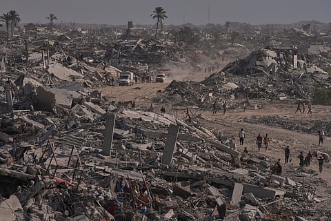 Displaced Palestinians walk through an area surrounded by destroyed buildings in Khan Younis, in the southern Gaza Strip, Saturday, Oct. 11, 2025, after Israel and Hamas agreed to a pause in their war and the release of the remaining hostages.