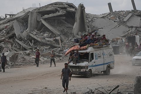 Displaced Palestinians ride on a van loaded with their belongings amid rubble in Gaza City, Sunday, Oct. 12, 2025, after Israel and Hamas agreed for a ceasefire
