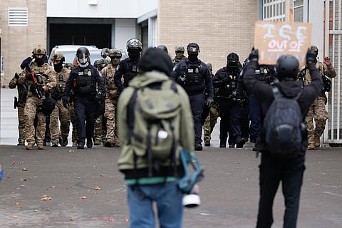 People protest outside a US Immigration and Customs Enforcement facility as law enforcement officers walk out of the gates to guard vehicles leaving the facility on Saturday, Oct. 11, 2025, in Portland, Ore.