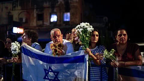 People carry flowers and Israeli flags upon the arrival of vehicles transporting the bodies of four hostages handed over following a ceasefire and prisoner exchange deal between Israel and Palestinian factions in Gaza, in front of the National Center for Forensic Medicine in Tel Aviv on October 13, 2025.