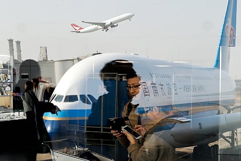 Passengers walk past a couple browsing their smartphones near a China Southern Airlines plane, parked on the tarmac at the Beijing Capital International Airport, Saturday, Nov. 19, 2016.