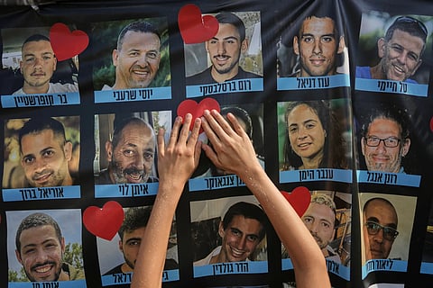 A person pastes a heart-shaped sticker on a banner with pictures of Israeli hostages during a a gathering at a plaza known as hostages square in Tel Aviv, Israel,