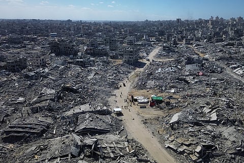 In this drone photo, Palestinians walk along a street surrounded by buildings destroyed during two years of Israeli army bombardments in Gaza City, Wednesday, Oct. 15, 2025.