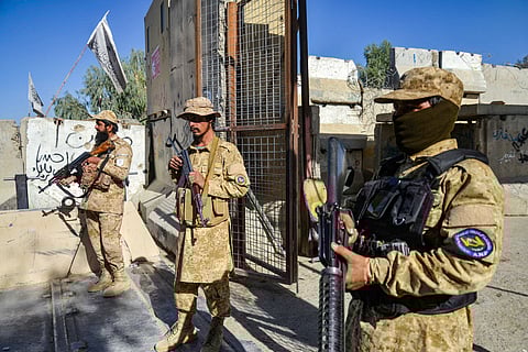 Taliban security personnel walk past a damaged car in the Spin Boldak district of Kandahar province on October 16, 2025, a day after the cross-border clashes between Afghanistan and Pakistan.