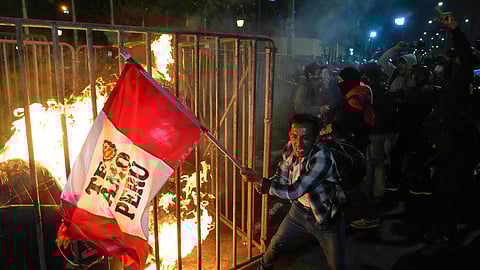 A demonstrator waves a Peruvian flag as a cardboard doll burns in front of Congress during a protest against new President Jose Jeri in Lima, Peru, Wednesday, Oct. 15, 2025.