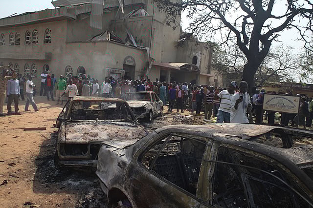 Onlookers gather around burnt-out cars at the site of a bomb blast at St. Theresa Catholic Church in Madalla, Nigeria, Sunday, Dec. 25, 2011.