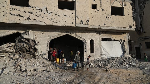 Displaced Palestinians collect water from a destroyed building in Khan Younis, Gaza Strip, Saturday, Oct. 18, 2025.