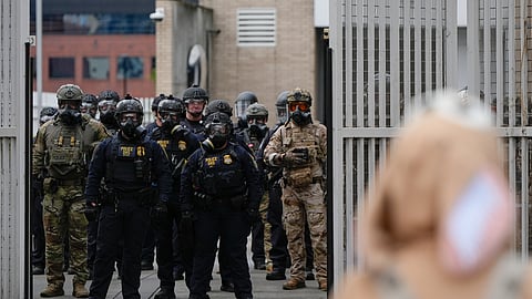 Law enforcement officers watch as the gates close at a U.S. Immigration and Customs Enforcement facility as people protest outside on Saturday, Oct. 11, 2025, in Portland, Ore