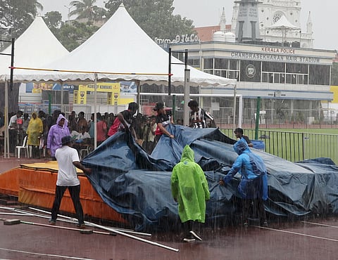 Officials cover the pole vault pit with tarpaulin sheets as heavy rain lashes the Chandrasekharan Nair Stadium in Thiruvananthapuram on Friday. The downpour interrupted the event of the State School Athletic Meet, for nearly an hour.
