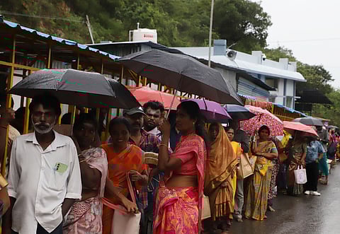 Devotees cover themselves from the rain while waiting for their turn to board the hill bus at the Maruthamalai Temple.