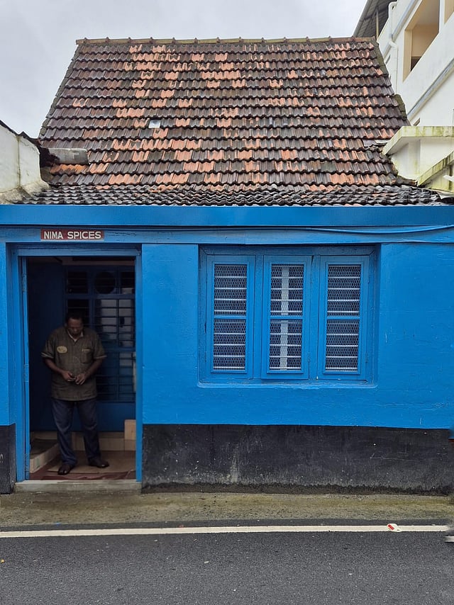 A building with Manglorean tiles lies wedged between two modern structures |