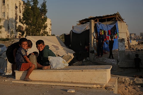 Palestinian children sit on a grave near makeshift tents for displaced people that were set up in a cemetery in Khan Younis, in the southern Gaza Strip, Friday, Oct. 31, 2025.