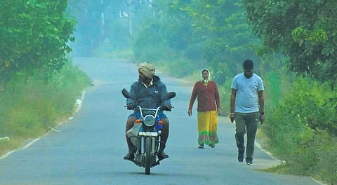 Early morning walkers and a motorcyclist make their way through a foggy road on the outskirts of Karimnagar.