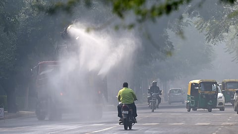 Commuters ride past an anti-smog gun spraying water to curb air pollution amid heavy smog conditions at Chanakya Puri in New Delhi