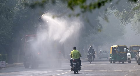 Commuters ride past an anti-smog gun spraying water to curb air pollution amid heavy smog conditions at Chanakya Puri in New Delhi on Thursday.