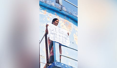 M Yakantha holds a placard demanding action against SI Upender atop a water tank in Thorrur on Wednesday
