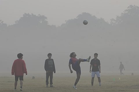 Youths play football amid air pollution smog at a garden in New Delhi.