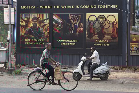 People ride past residential project boards featuring upcoming sports events, on the eve of the Commonwealth Sport General Assembly in Glasgow for formal approval of host city, in Ahmedabad, India.
