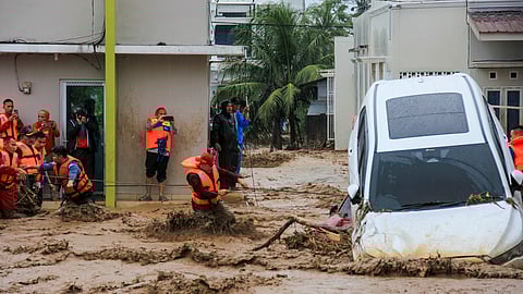 Rescuers wade through flood waters by holding a rope in their effort to evacuate residents who are trapped at their houses in Padang, West Sumatra province on November 27, 2025.