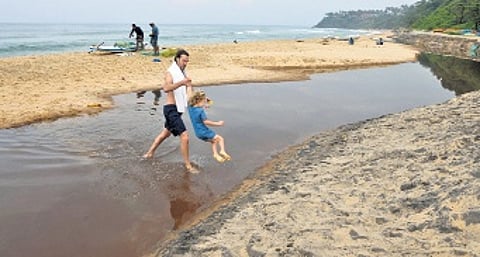 A tourist hauls his daughter out of the dirty, stinking stream of contaminated water flowing on the beach