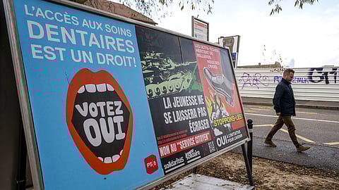 A person walks past referendum posters of political parties and associations as Swiss voters are casting ballots to decide whether women, like men, must do national service in the military, civil protection teams or in other forms, in Geneva, Switzerland, on Nov. 26, 2025.